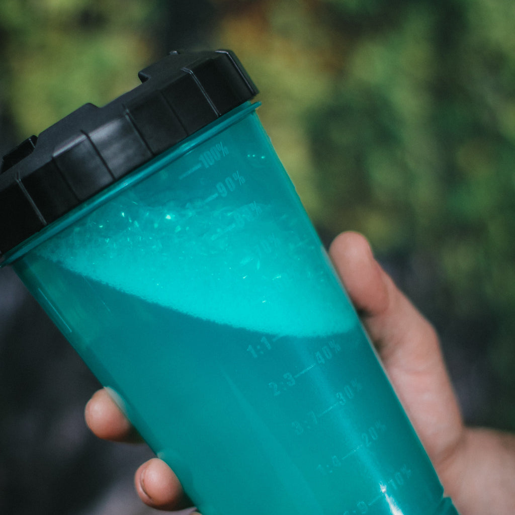 Hand holding a green beaker with a black lid.